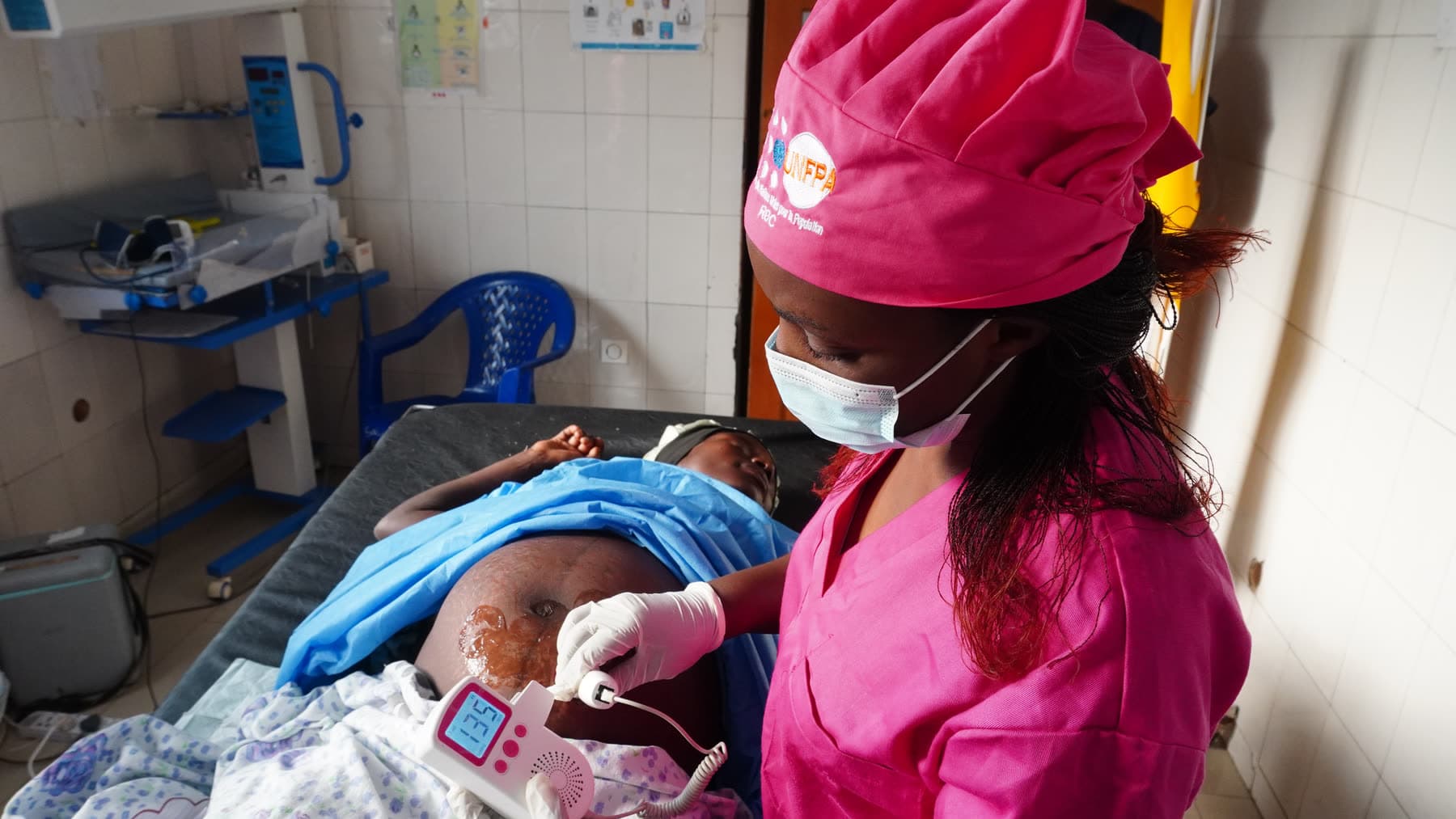 A clinician stands at the bedside in a DRC maternity ward, holding the eGov tablet that runs the platform